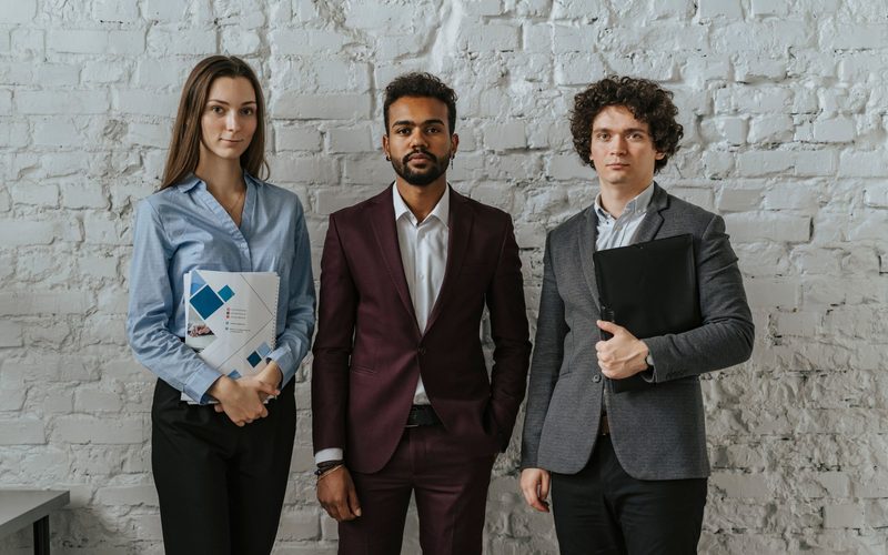 Three founders in business dress standing together against a white brick wall